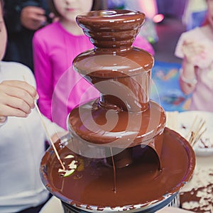 Vibrant Picture of Chocolate Fountain Fontain on childen kids birthday party with a kids playing around and marshmallows and fruit