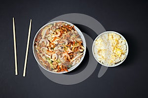 Vibrant plate of shrimp salad, bowl of rice with egg and chopsticks on black background. Take away food