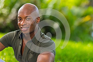 Vibrant portrait a handsome young African American man smiling at the camera. Man is posing outdoors in a park setting