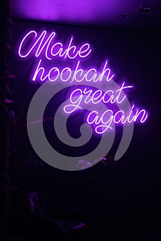 Vibrant purple neon sign with the words 'Make hookah great again' illuminated in a darkened room