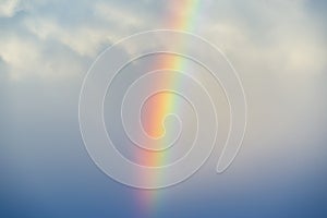 Vibrant rainbow against a misty stormy sky, white fluffy clouds