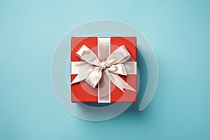 Vibrant red gift box decorated with white satin ribbon and bow, against a pastel blue backdrop