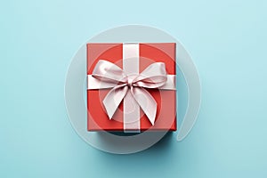 Vibrant red gift box decorated with white satin ribbon and bow, against a pastel blue backdrop