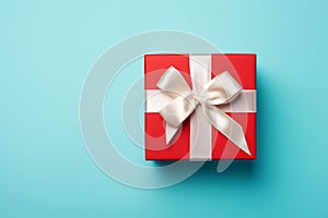 Vibrant red gift box decorated with white satin ribbon and bow, against a pastel blue backdrop