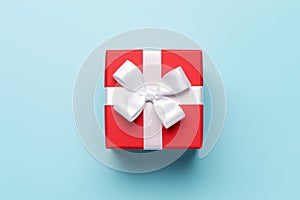 Vibrant red gift box decorated with white satin ribbon and bow, against a pastel blue backdrop