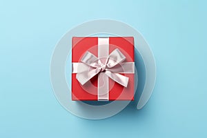 Vibrant red gift box decorated with white satin ribbon and bow, against a pastel blue backdrop