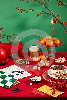 On a vibrant red and green backdrop, a go chess board, a glass of soft drink, plates of tangerines, sunflower seeds, colorful