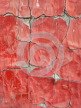 A vibrant red plaster is marred by deep cracks and erosion, showcasing the impact of time and elements on man-made