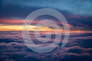 Vibrant red, purple and blue from sunset above the clouds from the window of a plane