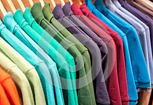 Vibrant shirts on hangs for sale in shop. Multicolored polo on wooden hanger. Summer fashion in department store
