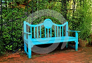 Vibrant turquoise blue colored wooden bench on terracotta brick pathway