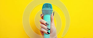 The vibrant turquoise microphone held by a stylish hand against a yellow backdrop..AI generated image