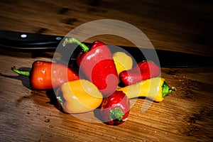 Vibrant Yellow, Red and Orange Sweet Peppers on a Bamboo Cutting surface covered in water drops, with a Chefâ€™s knife in the