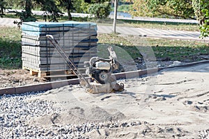 Vibrating plate compactor for sealing sand before laying tiles. Pallet with tiles on a city background