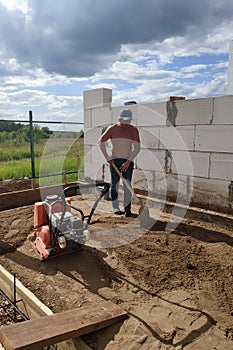 Vibrating plate in use, the worker with the help of a vibrating plate compacts the sand, building a house