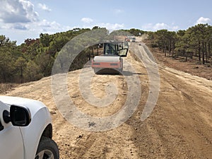 Vibrating roller compresses the soil of a road surface. Earthworks of highland forest road. Different types of machinery