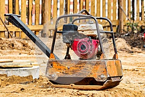 Vibratory plate compactor to firm soil at construction site, compact sand. Gasoline manual vibratory compactor for road works.