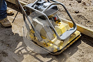 Vibratory plate compactor tool at construction compacting sand at sidewalk