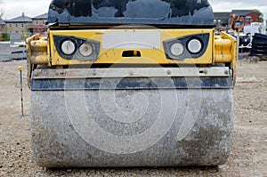 Vibratory road roller  broken front light compacting stone during road works on new housing development construction site