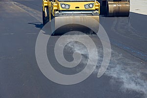 During vibratory road roller compactor process, a construction worker is operating the machine that lays new asphalt on