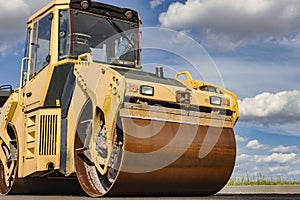 Vibratory road roller lays asphalt on a new road under construction. Close-up of the work of road machinery. Construction work on