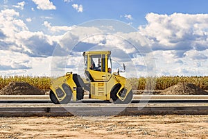 Vibratory road roller lays asphalt on a new road under construction. Close-up of the work of road machinery. Construction work on