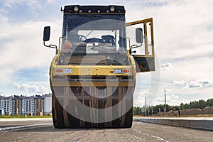 Vibratory road roller lays asphalt on a new road under construction. Close-up of the work of road machinery. Construction work on