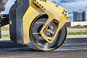 Vibratory road roller lays asphalt on a new road under construction. Close-up of the work of road machinery. Construction work on