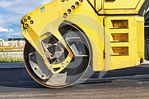 Vibratory road roller lays asphalt on a new road under construction. Close-up of the work of road machinery. Construction work on