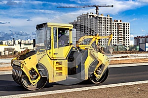 Vibratory road roller lays asphalt on a new road under construction. Close-up of the work of road machinery. Construction work on