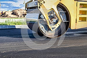 Vibratory road roller lays asphalt on a new road under construction. Close-up of the work of road machinery. Construction work on