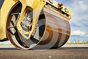 Vibratory road roller lays asphalt on a new road under construction. Close-up of the work of road machinery. Construction work on