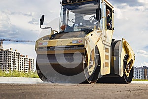 Vibratory road roller lays asphalt on a new road under construction. Close-up of the work of road machinery. Construction work on