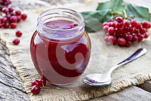 Viburnum fruit jam in a glass jar on a wooden table near the ripe red viburnum berries. Source of natural vitamins. Used in folk