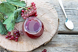 Viburnum fruit jam in a glass jar on a wooden table near the ripe red viburnum berries. Source of natural vitamins. Used in folk