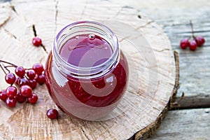 Viburnum fruit jam in a glass jar on a wooden table near the ripe red viburnum berries. Source of natural vitamins. Used in folk