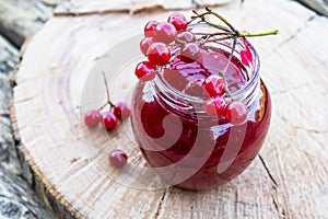 Viburnum fruit jam in a glass jar on a wooden table near the ripe red viburnum berries. Source of natural vitamins. Used in folk