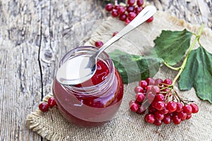 Viburnum fruit jam in a glass jar on a wooden table near the ripe red viburnum berries. Source of natural vitamins. Used in folk