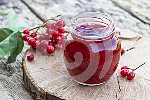 Viburnum fruit jam in a glass jar on a wooden table near the ripe red viburnum berries. Source of natural vitamins. Used in folk