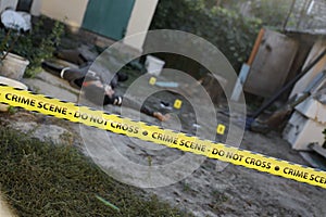 Victim of a violent crime in a backyard of residental house in evening. Dead man body under the yellow police line tape and