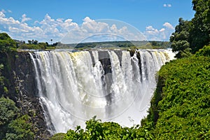 Victoria Falls with rainbow on Zambezi river, falling water from rock, view from Zambia, Africa