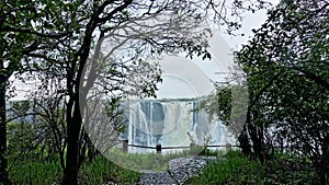 Victoria Falls, Zimbabwe. In the foreground is green grass, trees, a path, a fence in front of the precipice.