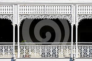 Victorian decorative wrought iron balcony with a plant on it but mostly darkness behind the white painted ornate railings -