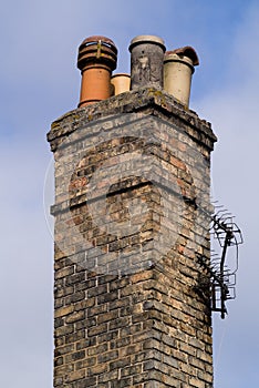 Victorian domestic chimney with four assorted chimney-pots against a clear blue sky background. Close up