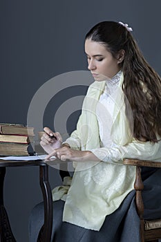 A Victorian or Edwardian woman sitting at a desk reading and writing with an ink dip pen