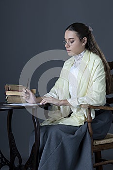 A Victorian or Edwardian woman sitting at a desk reading and writing with an ink dip pen