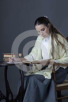 A Victorian or Edwardian woman sitting at a desk reading and writing with an ink dip pen