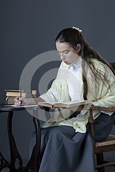 A Victorian or Edwardian woman sitting at a desk reading and writing with an ink dip pen