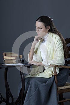 A Victorian or Edwardian woman sitting at a desk and writing with an ink dip pen