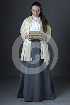 A Victorian or Edwardian woman standing and holding a pile of books